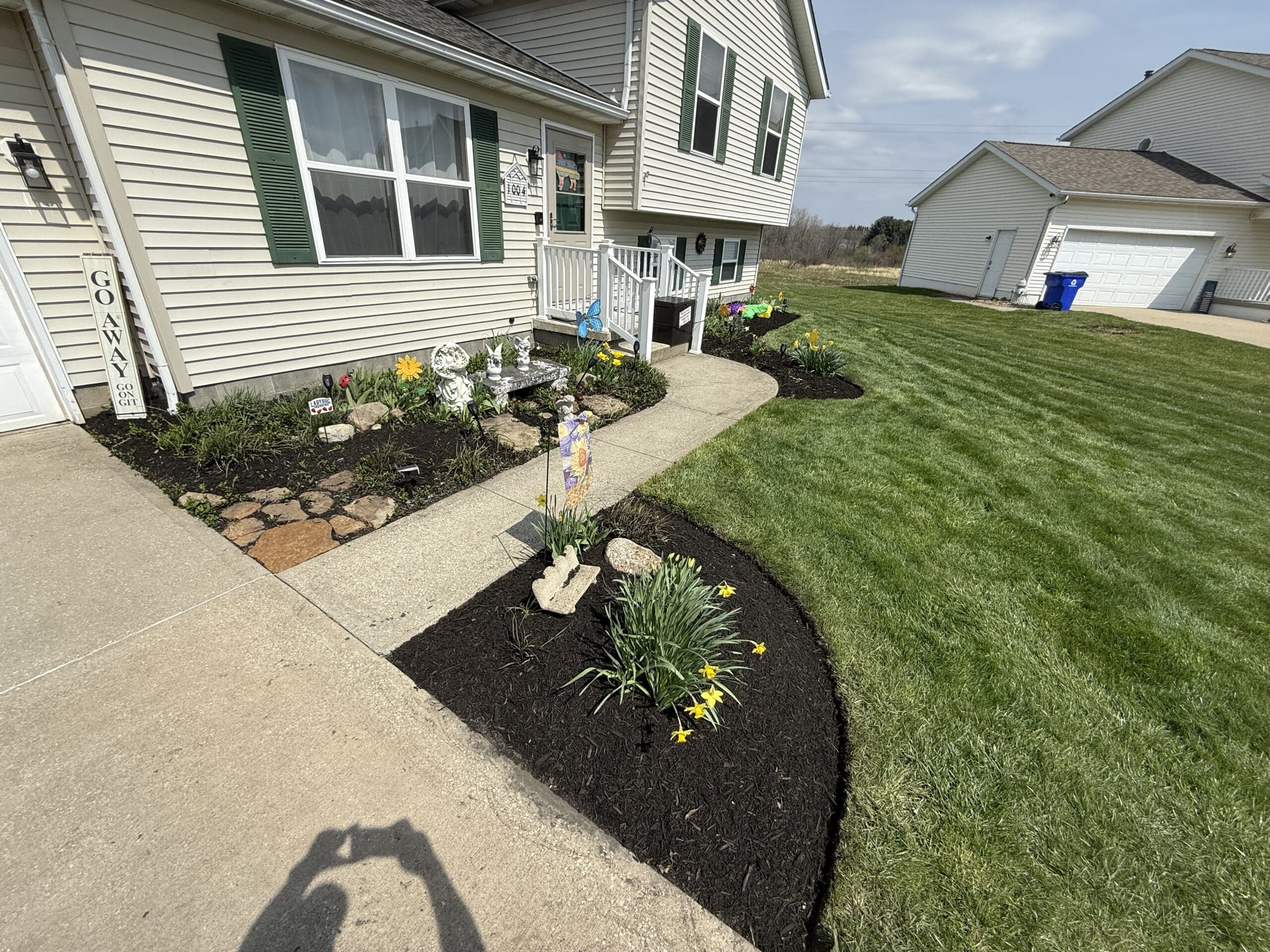 In front of a house, a clean cut trim of the yard has been completed. Mulching and flowers have been placed by Pro Finish Lawn Care, and the area shines with a glow.