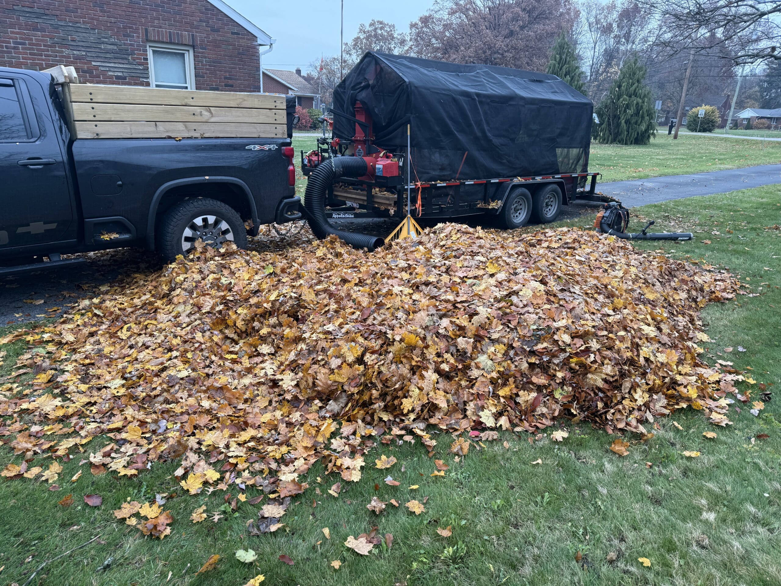 Beside a home's curb, a brilliant pile of orange and red leaves is stacked neatly after being collected by Pro Finish.